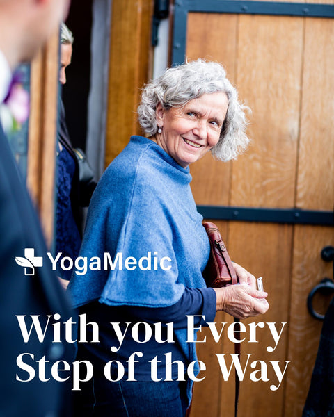 Woman in blue sweater standing in front of a wooden door with YogaMedic logo and text.