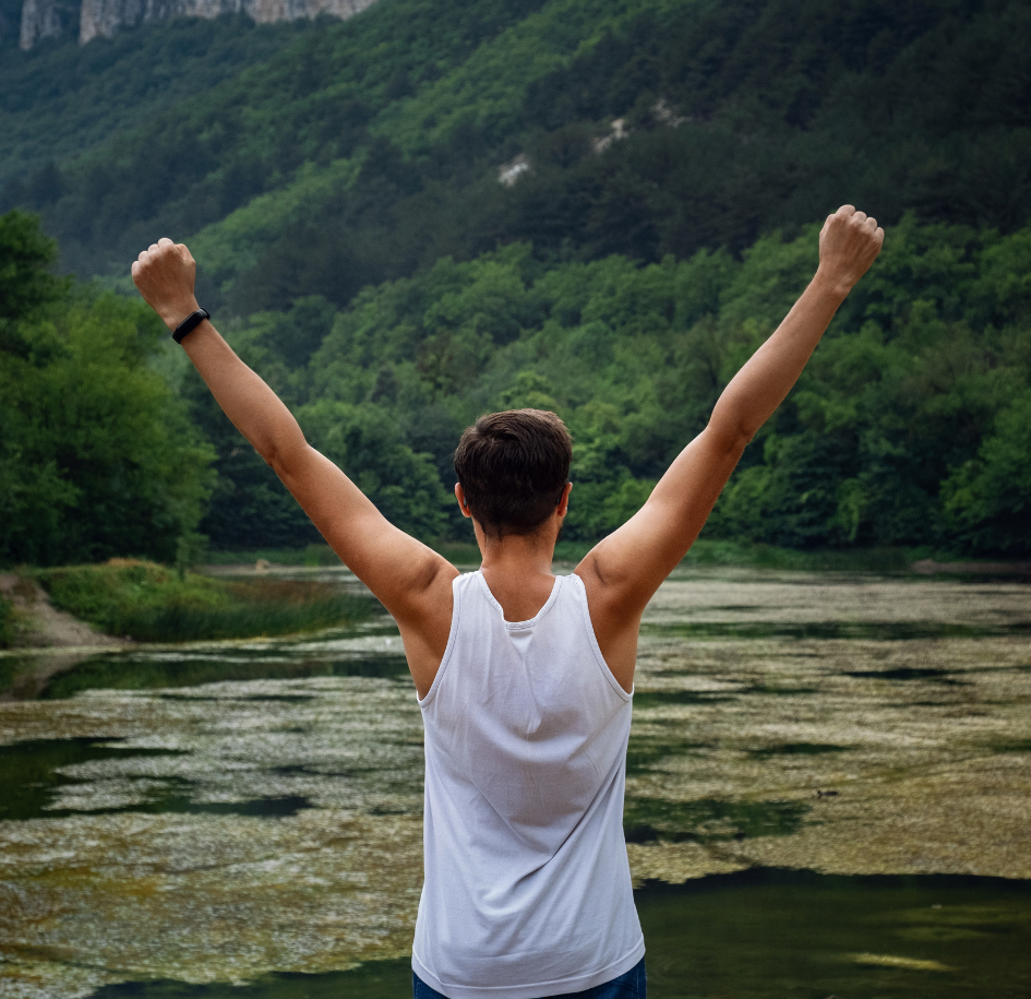 Person with arms raised in front of a scenic view with trees and water.